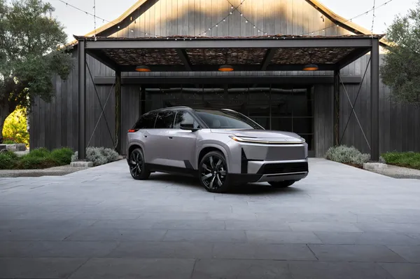 A silver 2027 Toyota Highlander EV parked in front of a modern vineyard barn structure at golden hour.