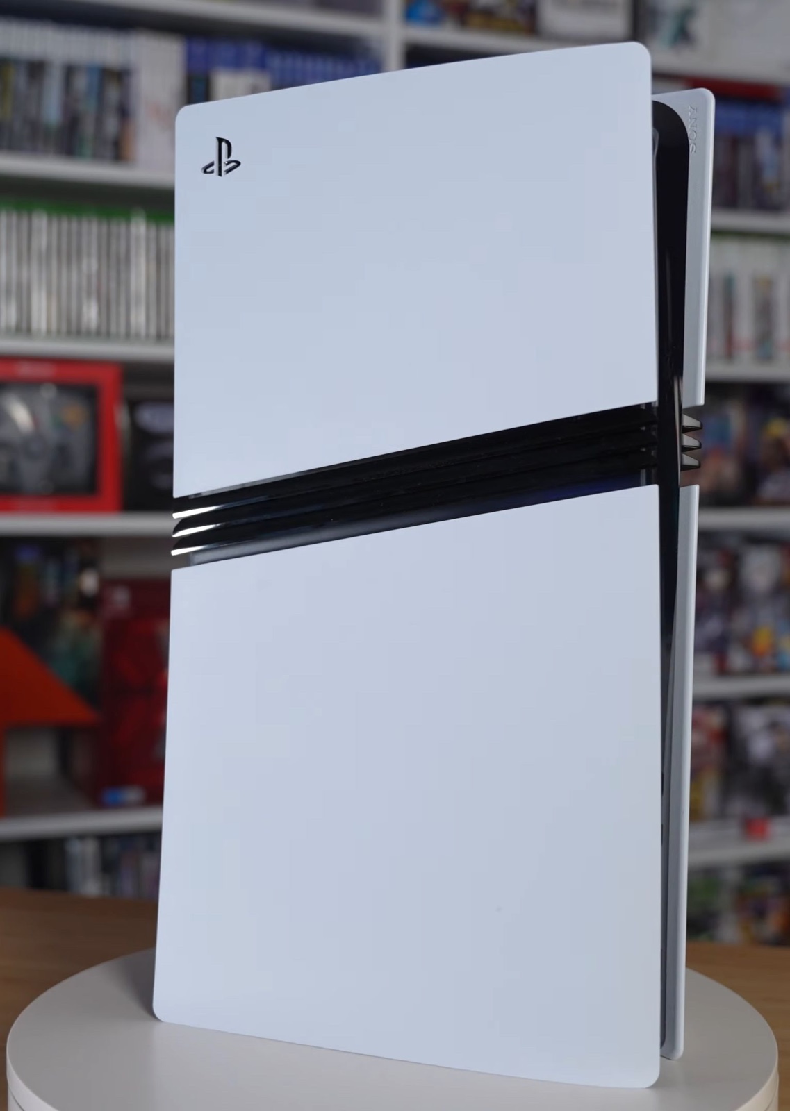 PlayStation 5 Pro console standing vertically in white, with shelves of games in the background