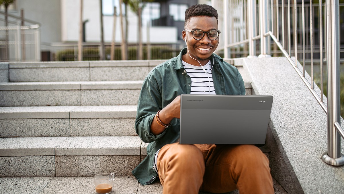 A student sitting on outdoor steps smiling during a video call on the Acer Chromebook Plus 514