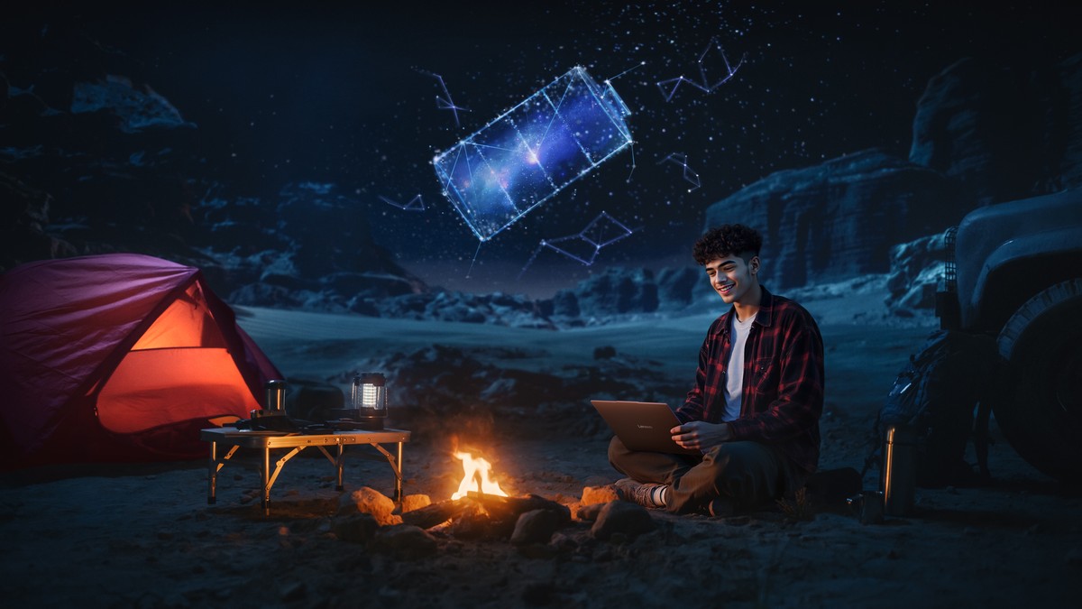A camper working on the IdeaPad Slim 3x beside a campfire at night, with a glowing battery-shaped constellation in the starry sky above