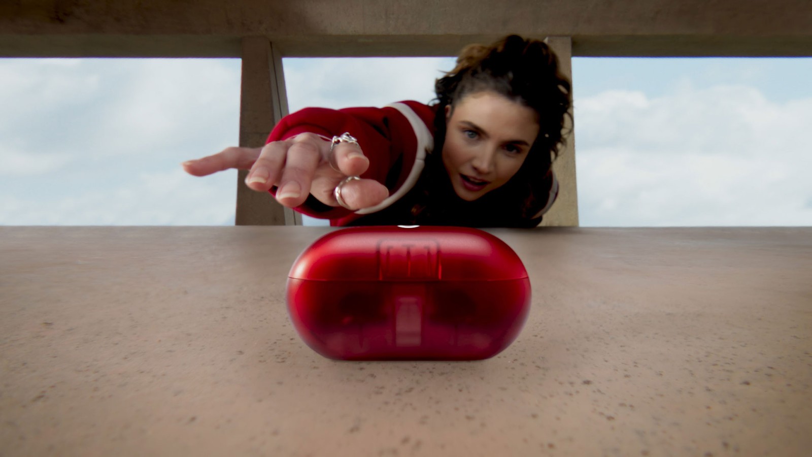 A woman reaches for the transparent red Beats Solo Buds charging case on a concrete ledge
