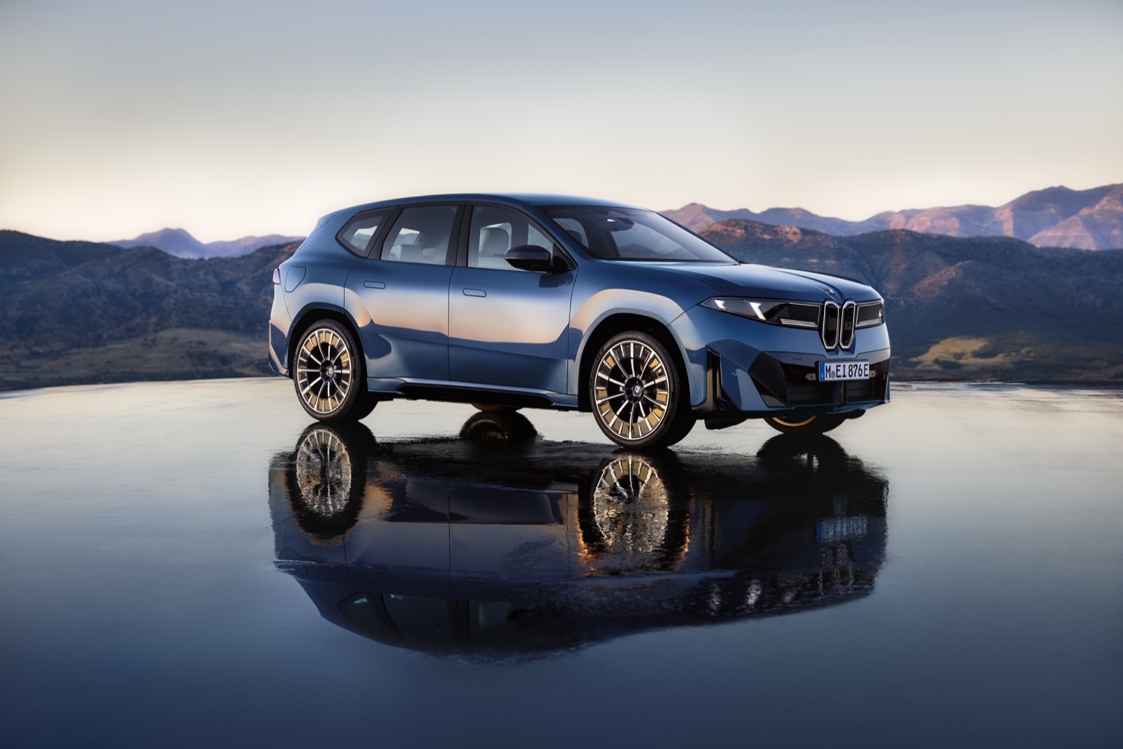 Blue BMW iX3 electric SUV parked with mountains behind, front three-quarter view