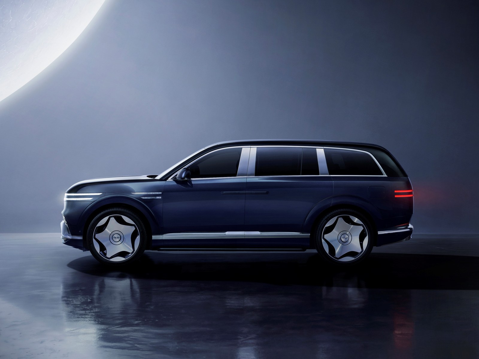 Dark blue Genesis GV90 flagship electric SUV in profile against a moonlit studio backdrop