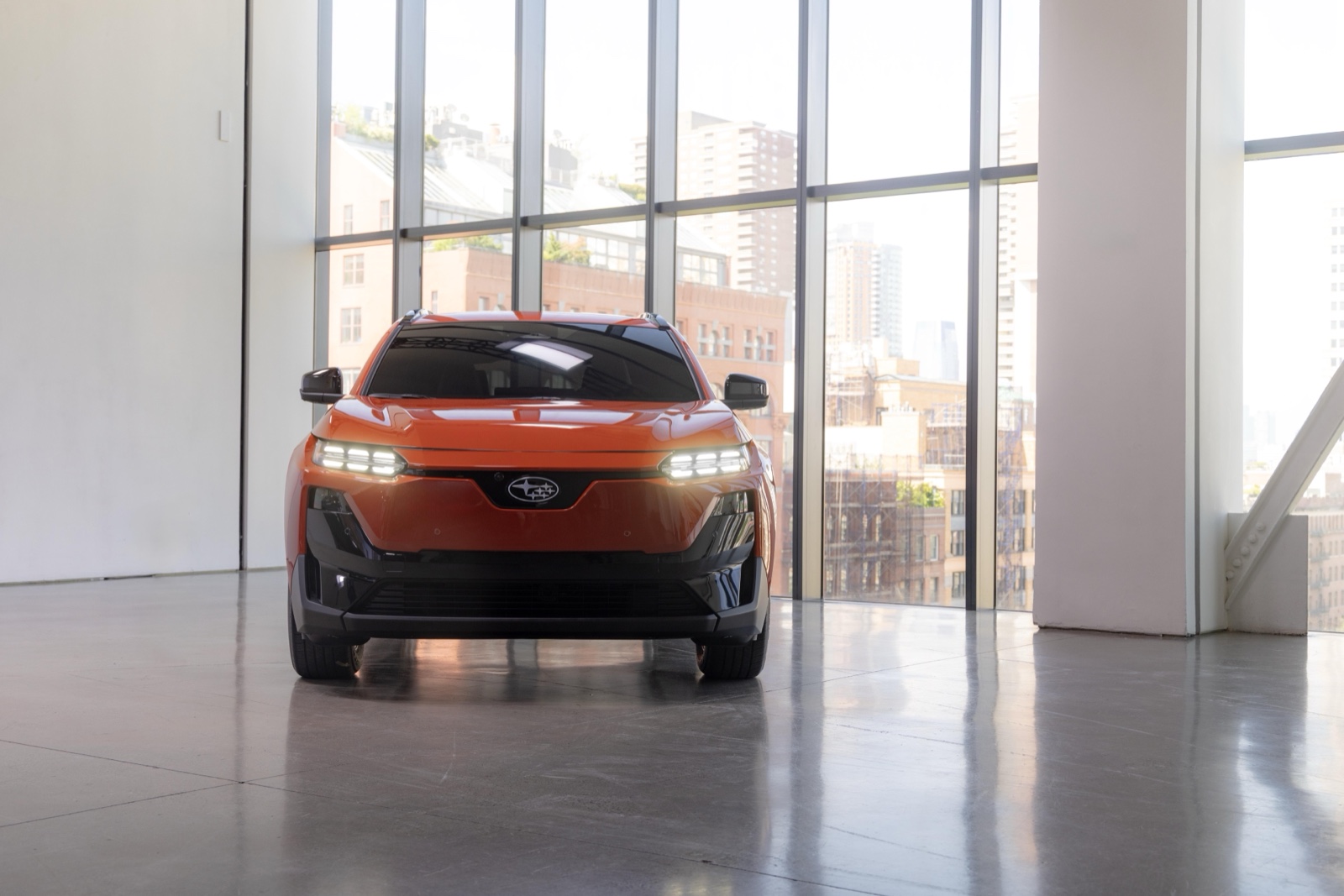 Orange 2026 Subaru Uncharted EV with New York skyline behind glass