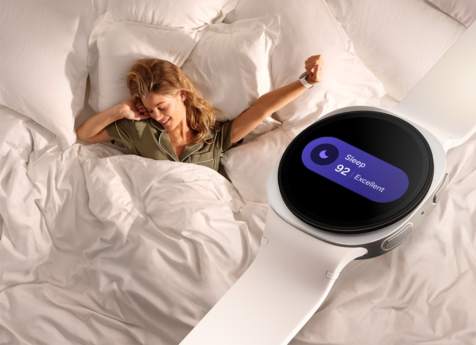 A woman stretches awake in bed wearing a Galaxy Watch 8 showing a sleep score of 92