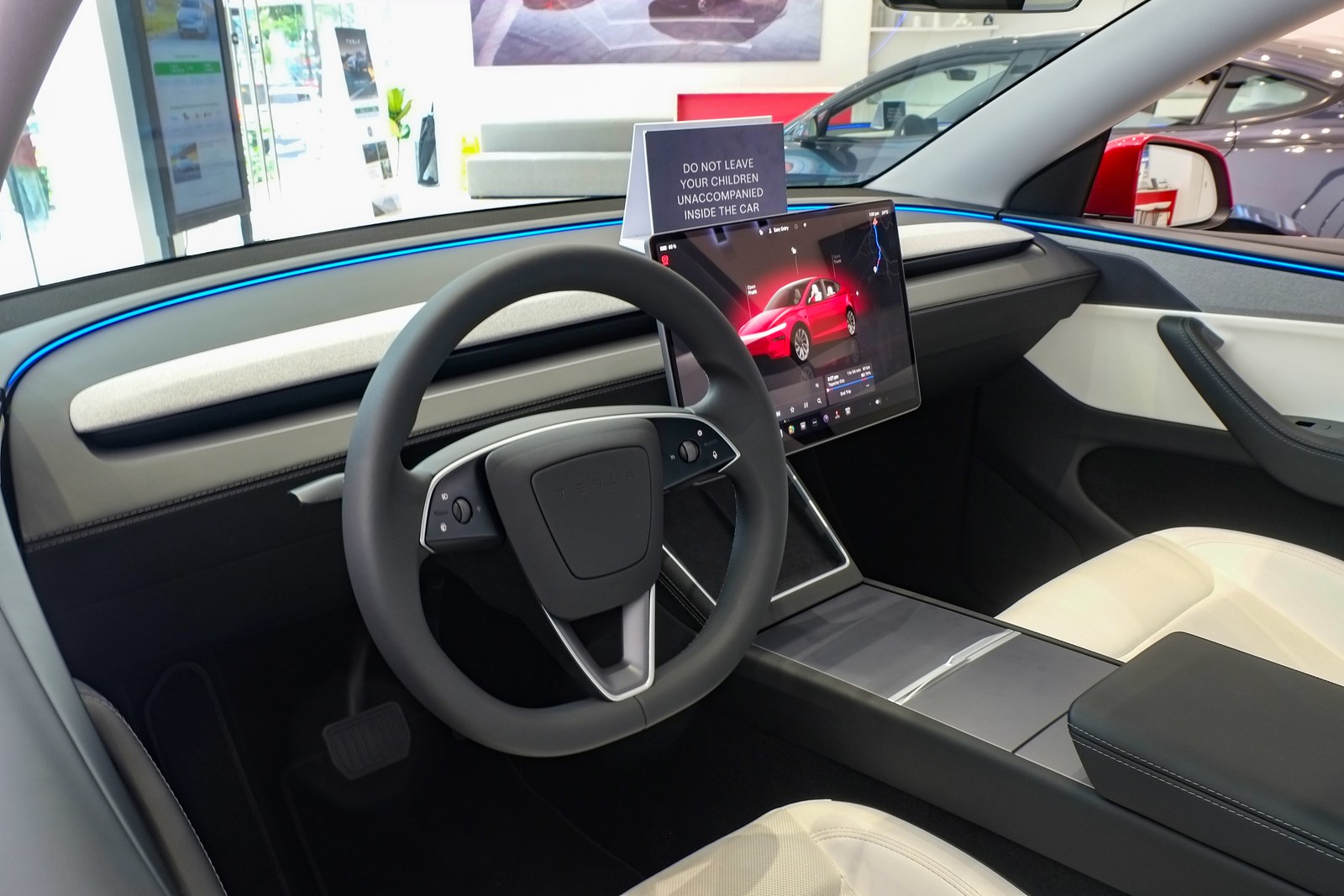 The driver's side of a 2025 Tesla Model Y in a showroom: steering wheel, center touchscreen, center console and the driver's footwell
