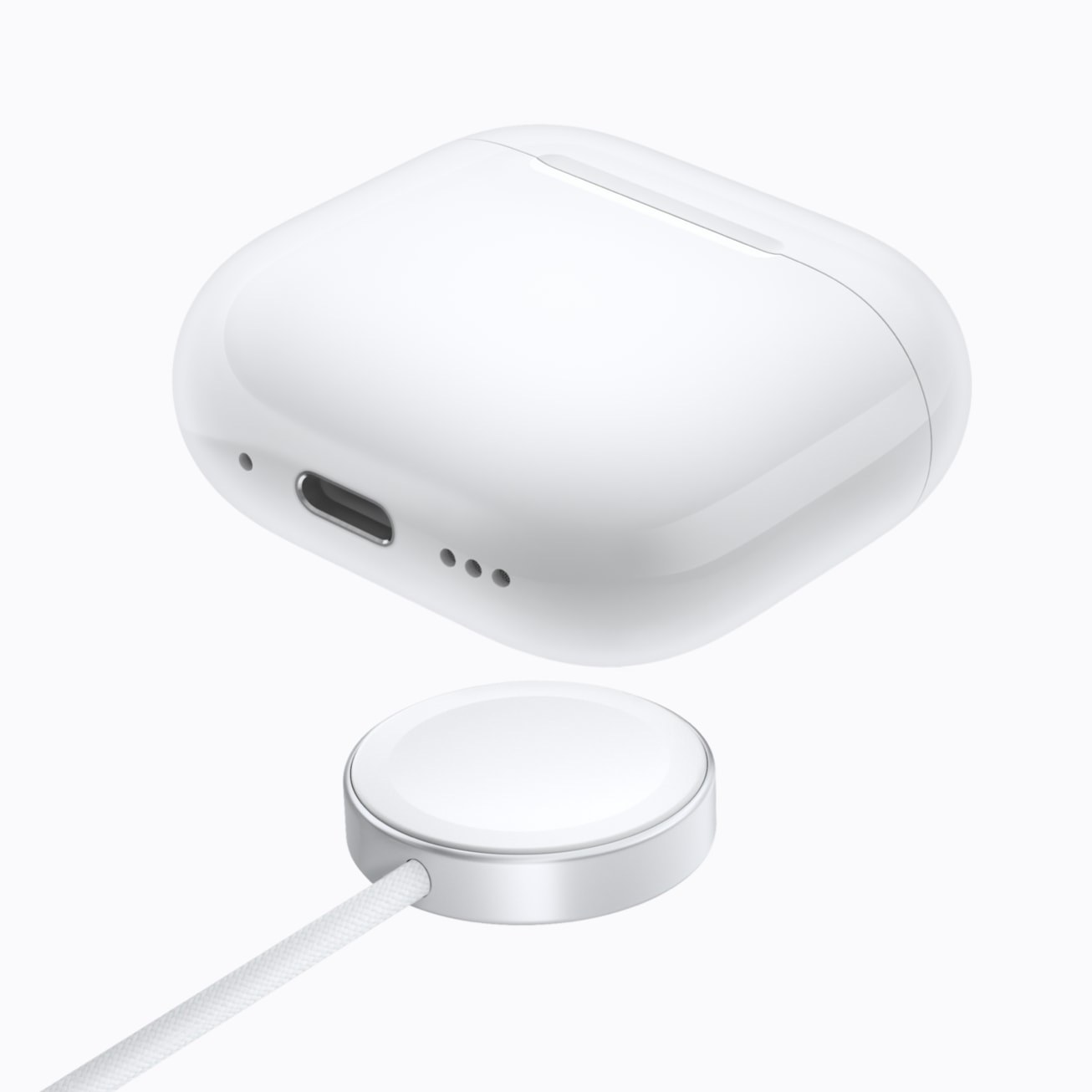 White AirPods 5 with Wireless Charging Case seen from below, showing its USB-C port above a round Apple Watch charger
